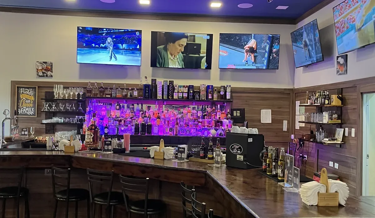 Inside 365 Sports Bar Juan Dolio — five screens showing live sport above the purple-lit backbar and the wooden bar counter